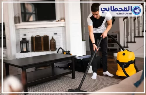 شركة تنظيف شقق بعنك 0548145142 القحطاني عامل تنظيف يستخدم جهاز شفط لتنظيف السجاد بعناية داخل غرفة المعيشة.