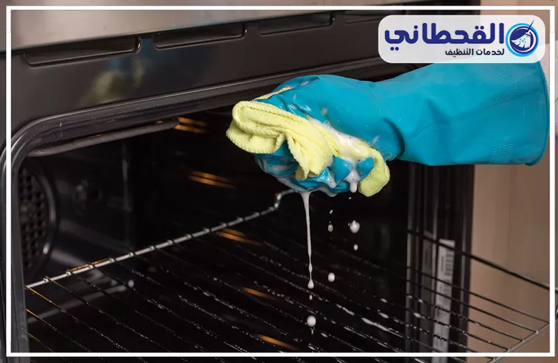 تنظيف الأفران بعد الإهمال الطويل بسيهات 0548145142 شركة القحطاني. يد مرتدية قفاز أزرق تعصر إسفنجة مبللة بالصابون أثناء تنظيف رفوف داخل فرن كهربائي مع تساقط قطرات رغوة تنظيف داخل الفرن.