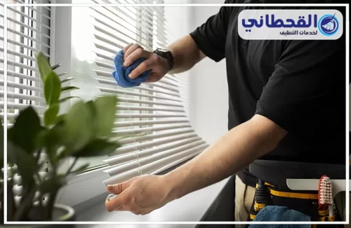 تنظيف ستائر رول بسيهات 0548145142 القحطاني فني يمسح النوافذ بقماش أزرق يوضح طريقة تنظيف ستائر الشرائح بدقة.