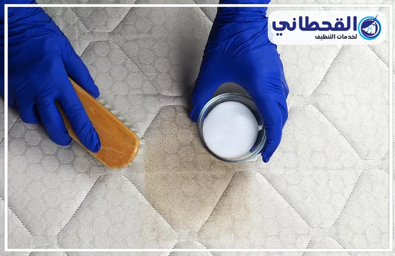 شركة غسيل مراتب السرير بسيهات 0548145142 القحطاني فني يرتدي قفازات زرقاء يستخدم فرشاة ومسحوق لغسيل مراتب السرير بسيهات لإزالة البقع.