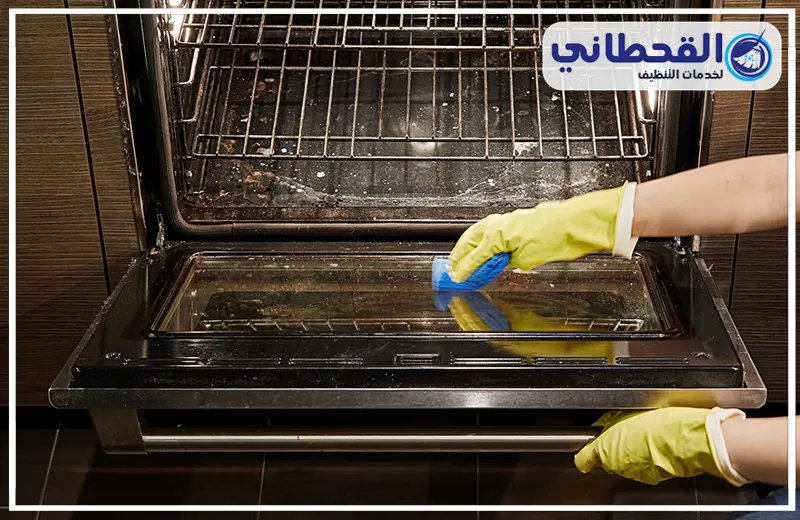 تنظيف زجاج الفرن بسيهات 0548145142 شركة القحطاني. يدان ترتديان قفازات صفراء تستخدمان إسفنجة زرقاء لمسح وتنظيف الزجاج الداخلي لباب فرن كهربائي مفتوح مع وجود رفوف داخلية.