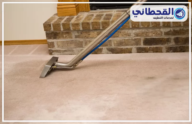تعقيم السجاد للمنازل التي فيها أطفال بصفوى 0548145142 شركة القحطاني. رأس ماكينة تنظيف سجاد فوق سجادة بيج داخل غرفة، مع ظهور خرطوم أزرق ويد معدنية ودرج حجري بالطوب وشعار القحطاني أعلى الصورة.