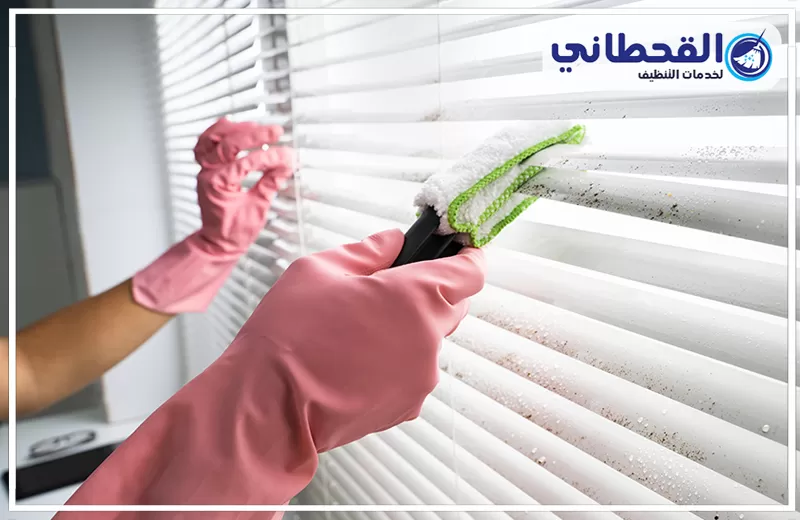 تنظيف ستائر بدون فك برأس تنورة 0548145142 شركة القحطاني. يدان بقفازات وردية تنظفان شرائح ستائر بيضاء بأداة مايكروفايبر مع شعار القحطاني أعلى الصورة