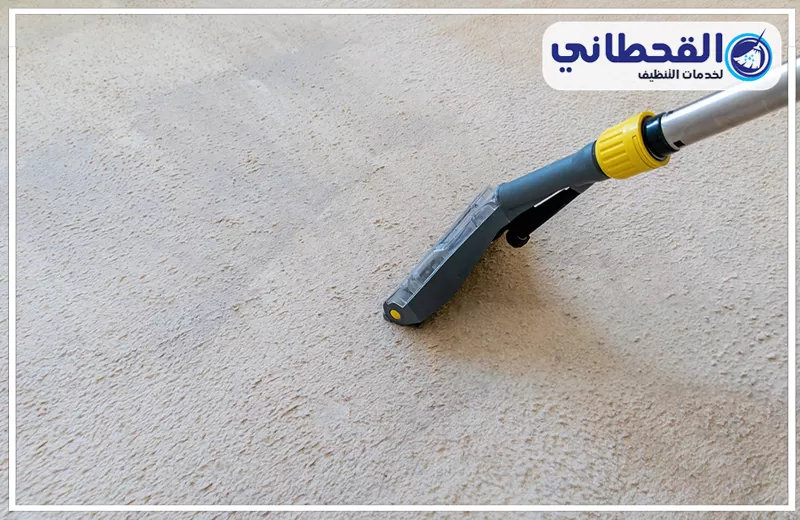 تنظيف الموكيت الثابت والأرضي بصفوى 0548145142 شركة القحطاني. رأس جهاز تنظيف وشفط فوق سجادة فاتحة اللون، مع ظهور بقعة رطبة أثناء التنظيف وشعار القحطاني أعلى الصورة.