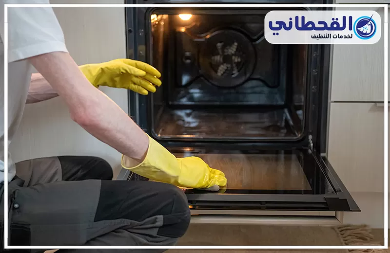 تنظيف باب الفرن الزجاجي بعنك 0548145142 شركة القحطاني عامل تنظيف يرتدي قفازات ويمسح باب الفرن من الداخل، مع إبراز تنظيف الأفران وإزالة آثار الدهون.