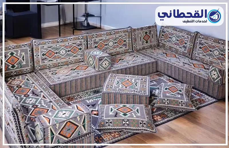 تنظيف المجالس الأرضية بعنك 0548145142 شركة القحطاني. مجلس عربي أرضي رمادي مزخرف، يحتوي على مساند ووسائد وطاولات قماشية وسجادة منقوشة، مع شعار القحطاني أعلى الصورة.