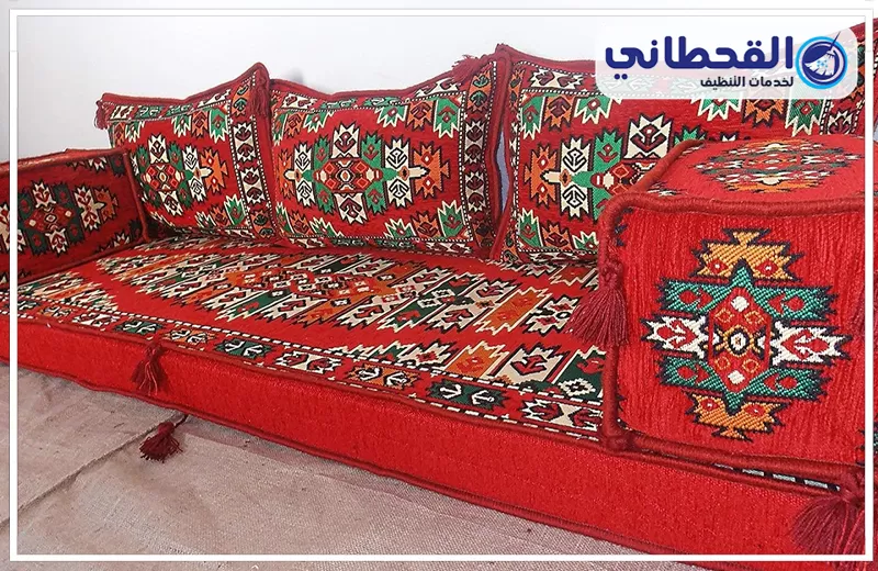 تنظيف الاثاث المجالس بسيهات 0548145142 شركة القحطاني مجلس عربي أرضي باللون الأحمر مزخرف بنقوش تراثية، يظهر بتصميم مرتب ومساند جانبية مناسبة لجلسات الضيافة.