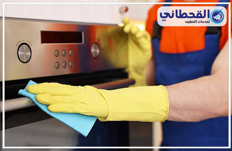تنظيف أفران غاز بعنك 0548145142 شركة القحطاني عامل تنظيف يمسح واجهة فرن استيل بقطعة قماش، مع إبراز خدمة تنظيف الأفران وإزالة الدهون والبقع.