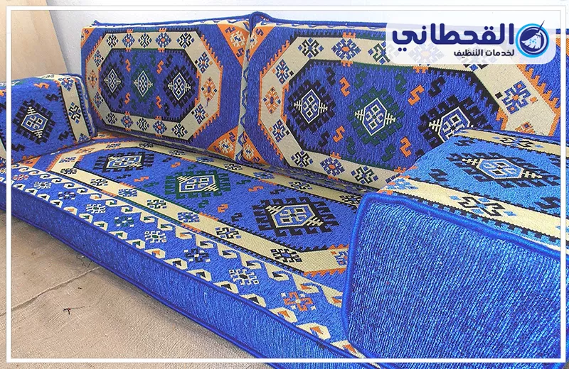 تنظيف كنب المجالس بعنك 0548145142 شركة القحطاني. كنب مجلس عربي باللون الأزرق مزخرف بنقوش تراثية، يحتوي على مساند ظهر وذراع جانبي وأقمشة منقوشة بدرجات الأزرق والبرتقالي والأبيض، مع شعار القحطاني أعلى الصورة.
