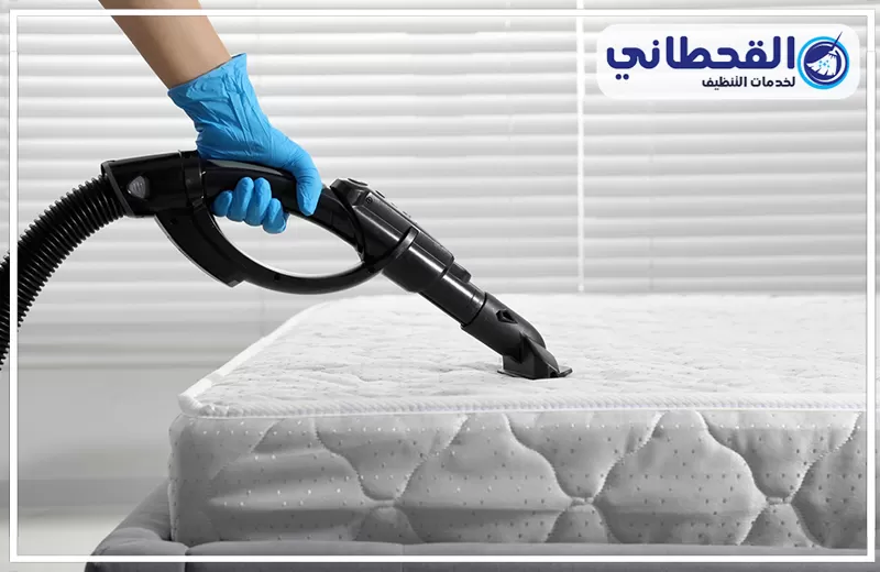 غسيل مراتب السرير بالبخار في الخبر 0548145142 شركة القحطاني عامل تنظيف يستخدم جهاز شفط عميق لتنظيف مرتبة سرير، مع ظهور شعار القحطاني لخدمات التنظيف.