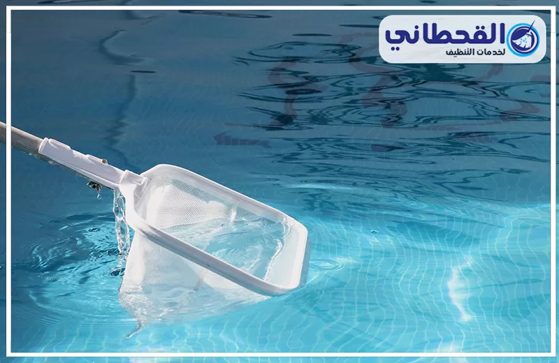 غسيل مسابح بالظهران 0548145142 شركة القحطاني. شبكة يدوية بيضاء لإزالة الشوائب داخل مسبح أزرق صافٍ، مع تموجات خفيفة بالمياه وظهور بلاط المسبح من الأسفل.