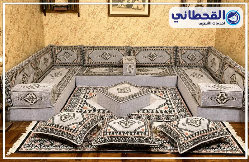 تنظيف مجالس قماش بالظهران 0548145142 شركة القحطاني. مجلس عربي رمادي مزخرف مع وسائد أرضية وسجادة منقوشة وطاولة وسط وشعار القحطاني للتنظيف.