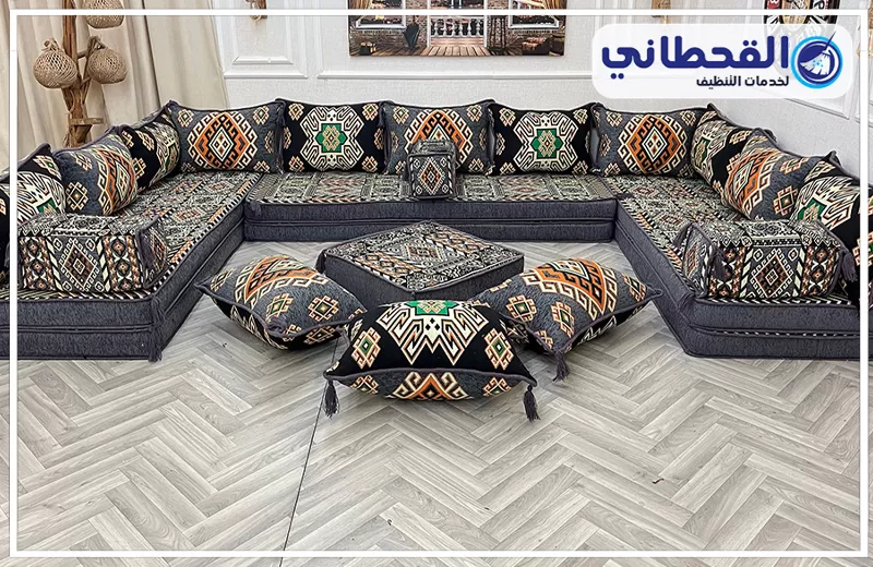 عامل تنظيف مجالس في سيهات 0548145142 شركة القحطاني مجلس أرضي واسع بتصميم تراثي داكن، مزود بمساند مزخرفة وطاولة وسط، ويظهر مرتبًا داخل غرفة أنيقة.